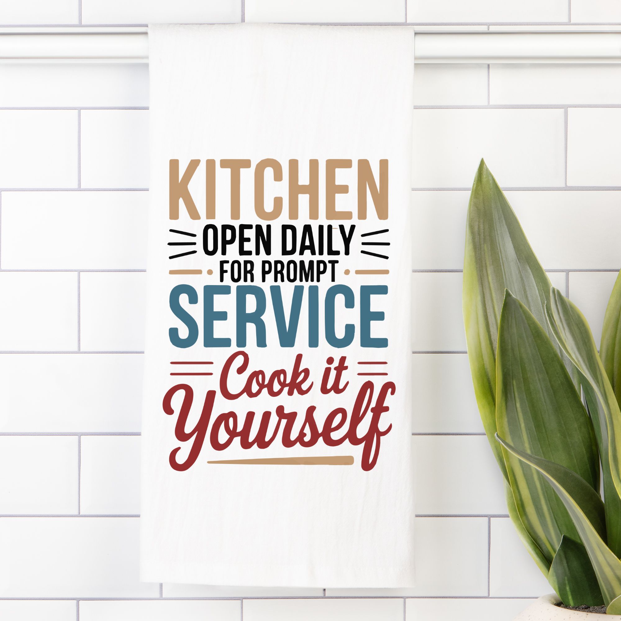 Colorful text on a white tea towel with a plant to the right.