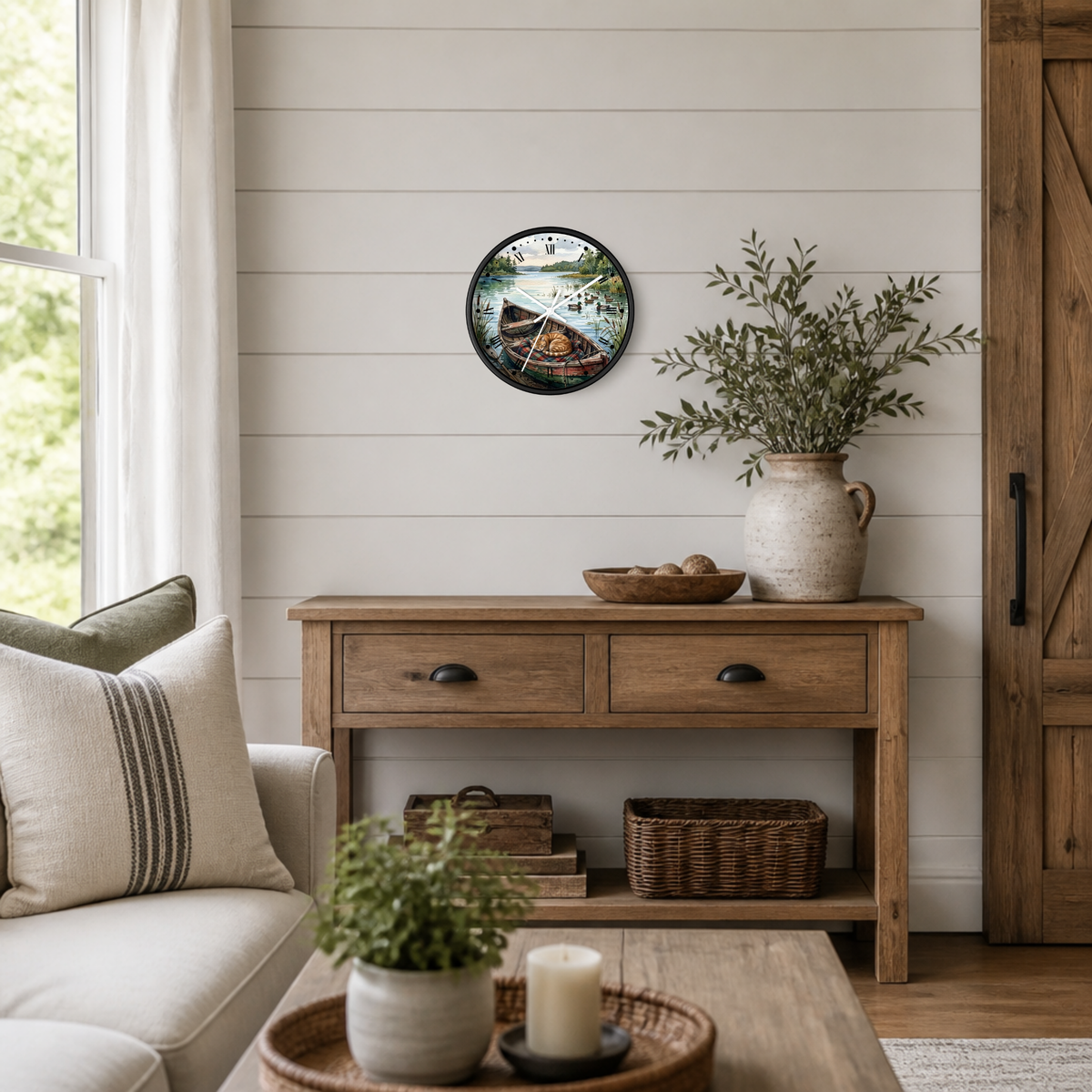 A round wall clock with a rustic illustration of a cat sleeping in a boat on a the water with ducks in the distance, hanging on a white shiplap wall above a wooden console table in a styled living room.