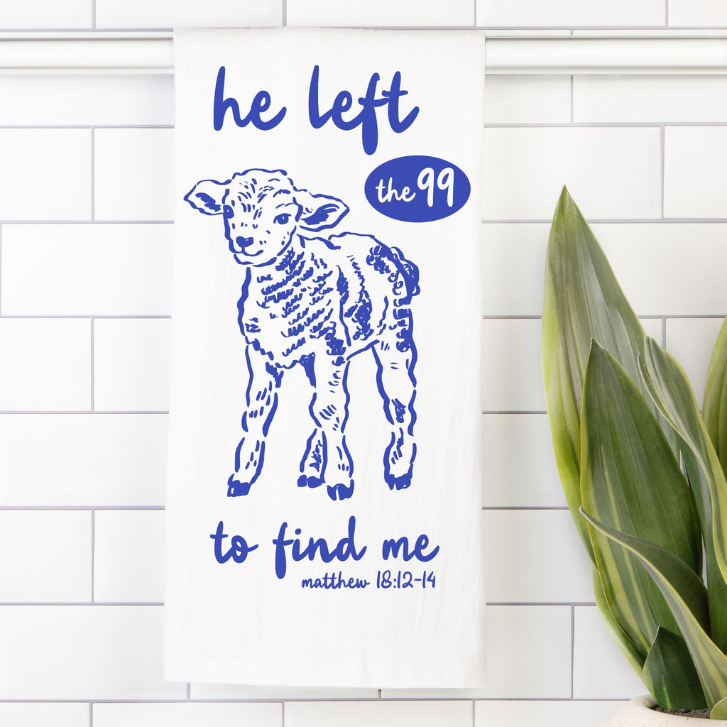 Tea Towel with a blue illustration of a lamb with text on a white tiled wall with a plant.