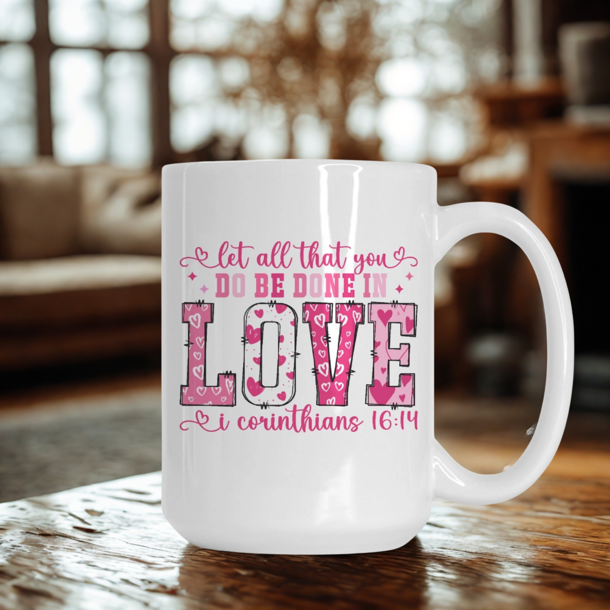 White mug with pink text on a wooden table in a blurred indoor setting