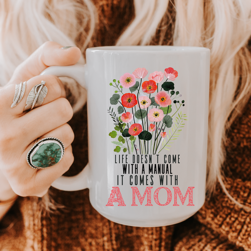 15 oz white mug with floral design and text held by a person wearing rings, on a textured fabric background.