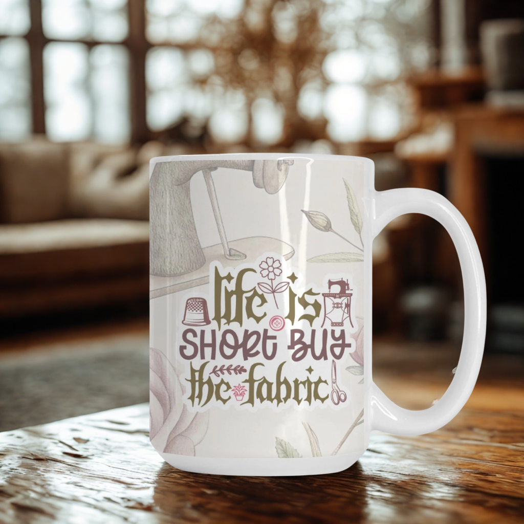 White mug with 'life is short, buy the fabric' text on a wooden table in a cozy room.