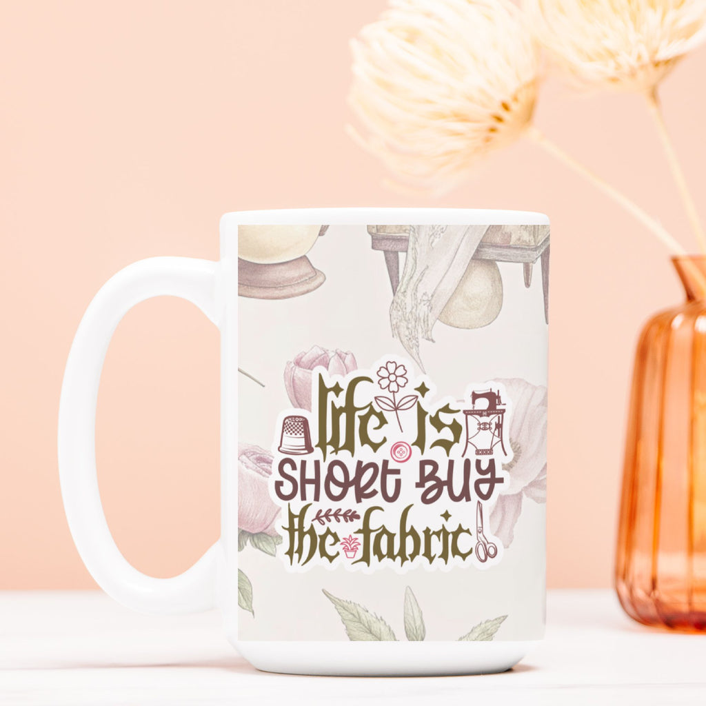 White mug with 'life is short, buy the fabric' text on a light pink background