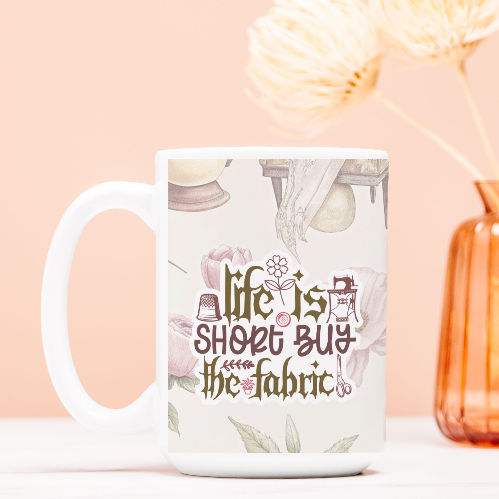 White mug with 'life is short, buy the fabric' text on a light pink background