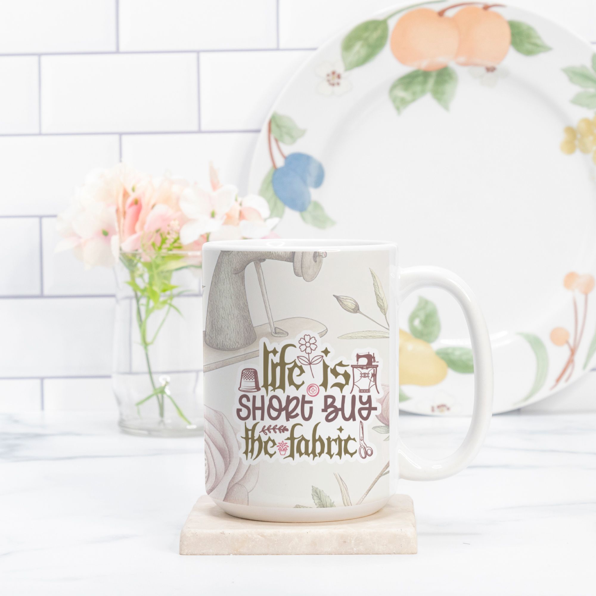 Mug with 'life is short, buy the fabric' quote and floral design on a white surface.