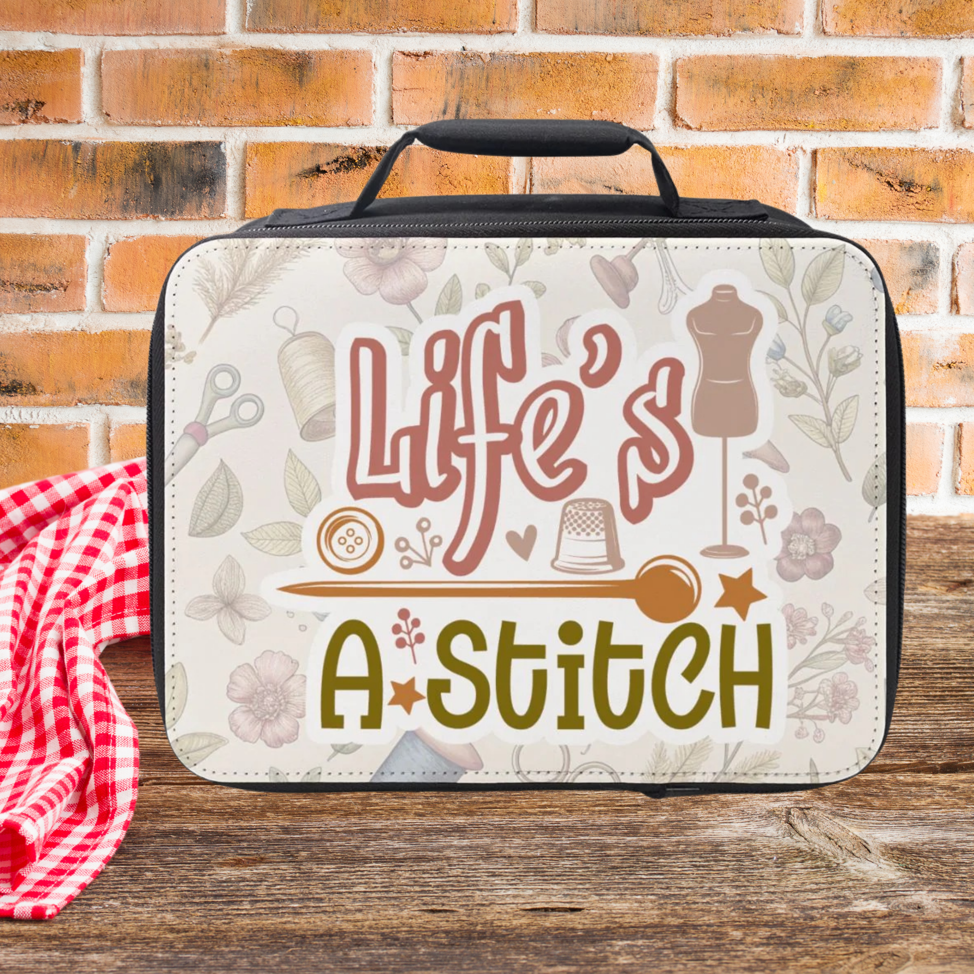 Insulated lunch bag with 'Life's a Stitch' text and sewing-themed design on a wooden picnic table with brick background.