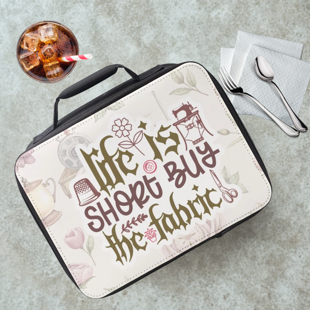 Lunch bag with 'Life is short, buy the fabric' text on a cafeteria table with a drink and utensils.