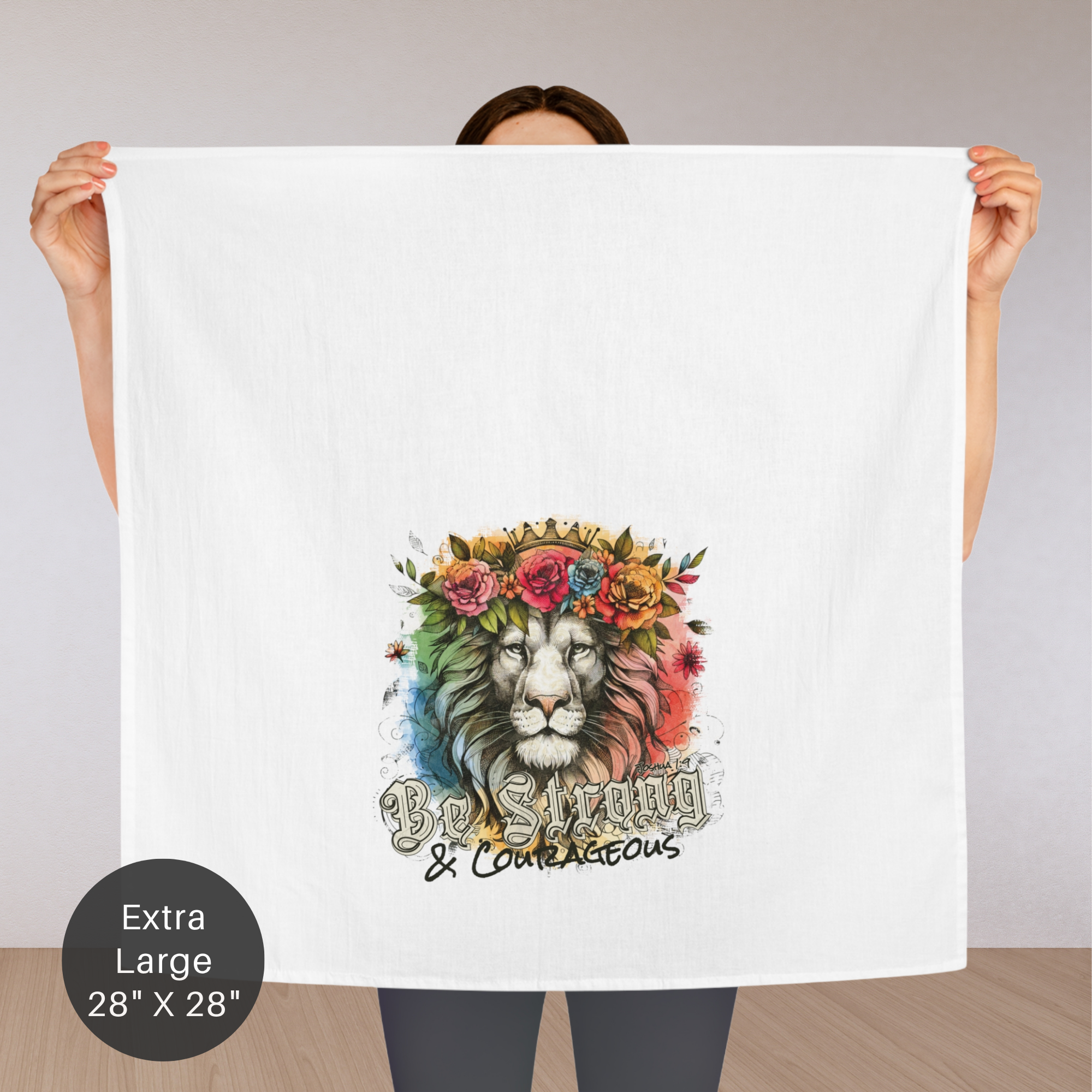 Person holding a large white towel with a colorful lion design and text 'Be Strong & Courageous'.