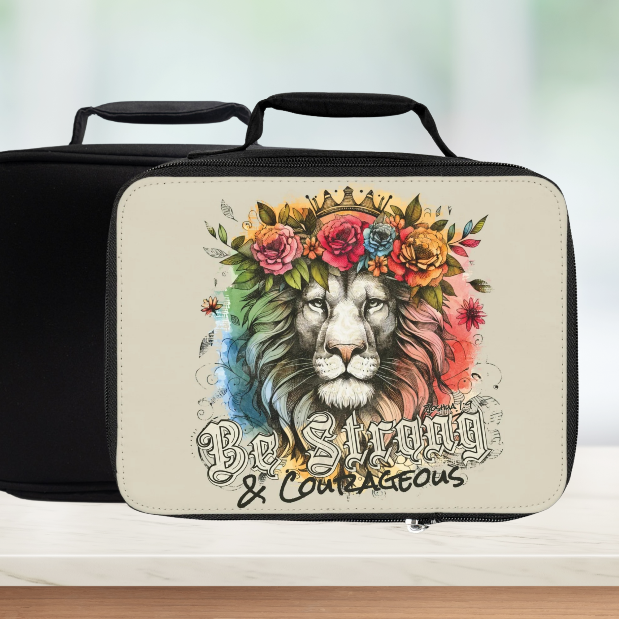 Lunch bag with a lion design and 'Be Strong & Courageous' text on a blurred background