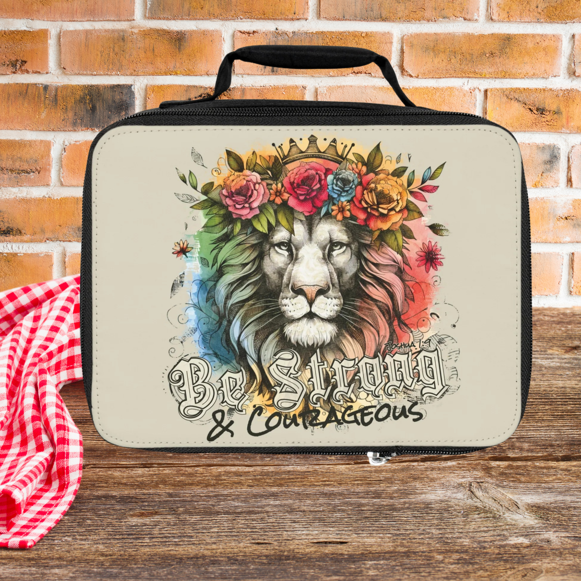 Lunch bag with lion design and floral crown on a wooden picnic table against brick wall background