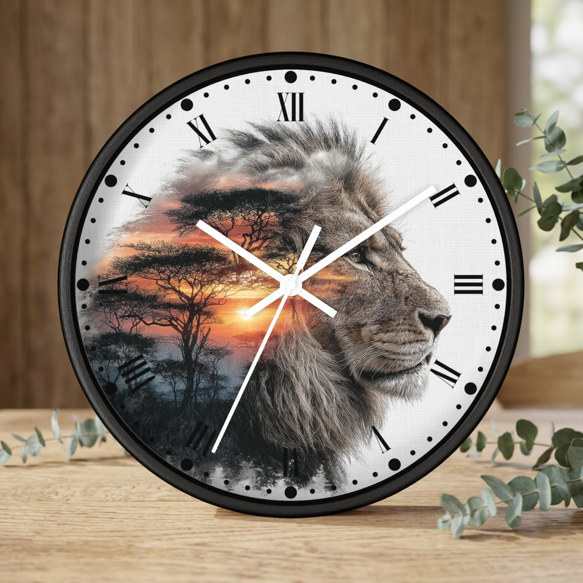 A round wall clock with a black frame and a printed design of a lion head over an African savanna sunset scene, styled on a wooden surface with eucalyptus leaves.
