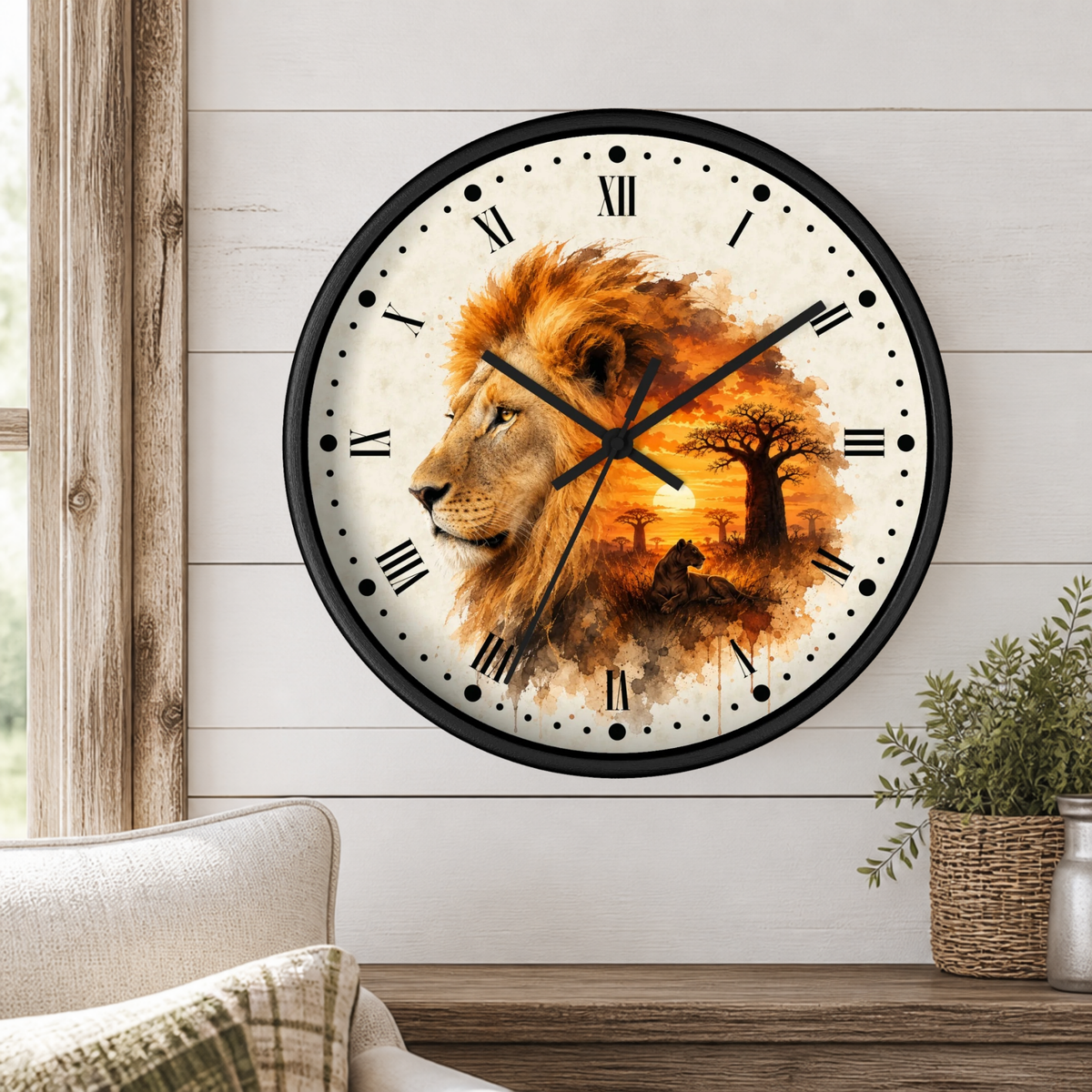 A round wall clock with a black frame and Roman numerals, featuring a watercolor-style lion and savanna scene on the face, mounted on a white shiplap wall above a wooden table with a plant.