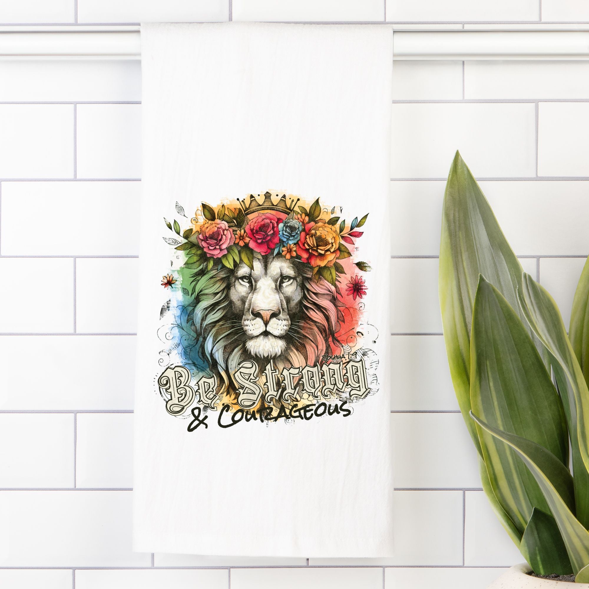 Decorative tea towel with a lion wearing a floral crown and 'Be Strong & Courageous' text on a white tiled wall.