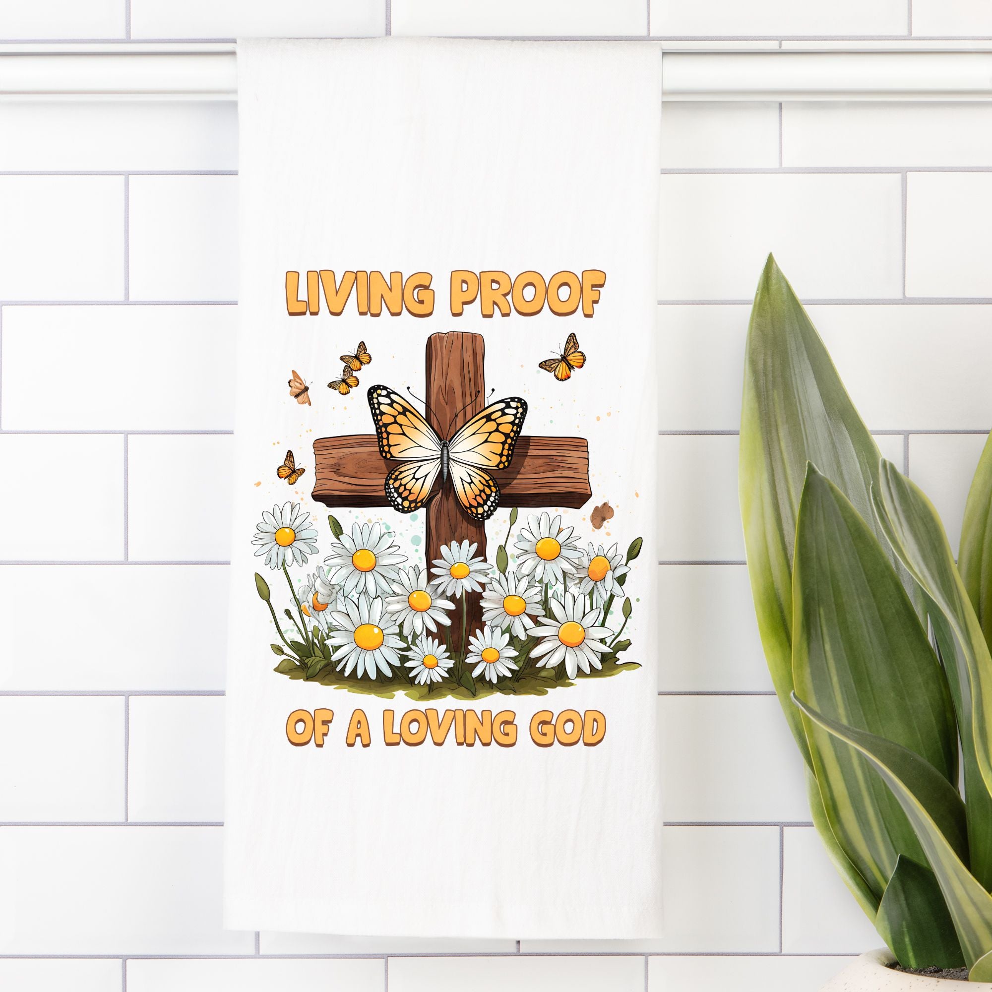 Decorative tea towel with a cross, flowers, and butterflies on a white tiled wall.