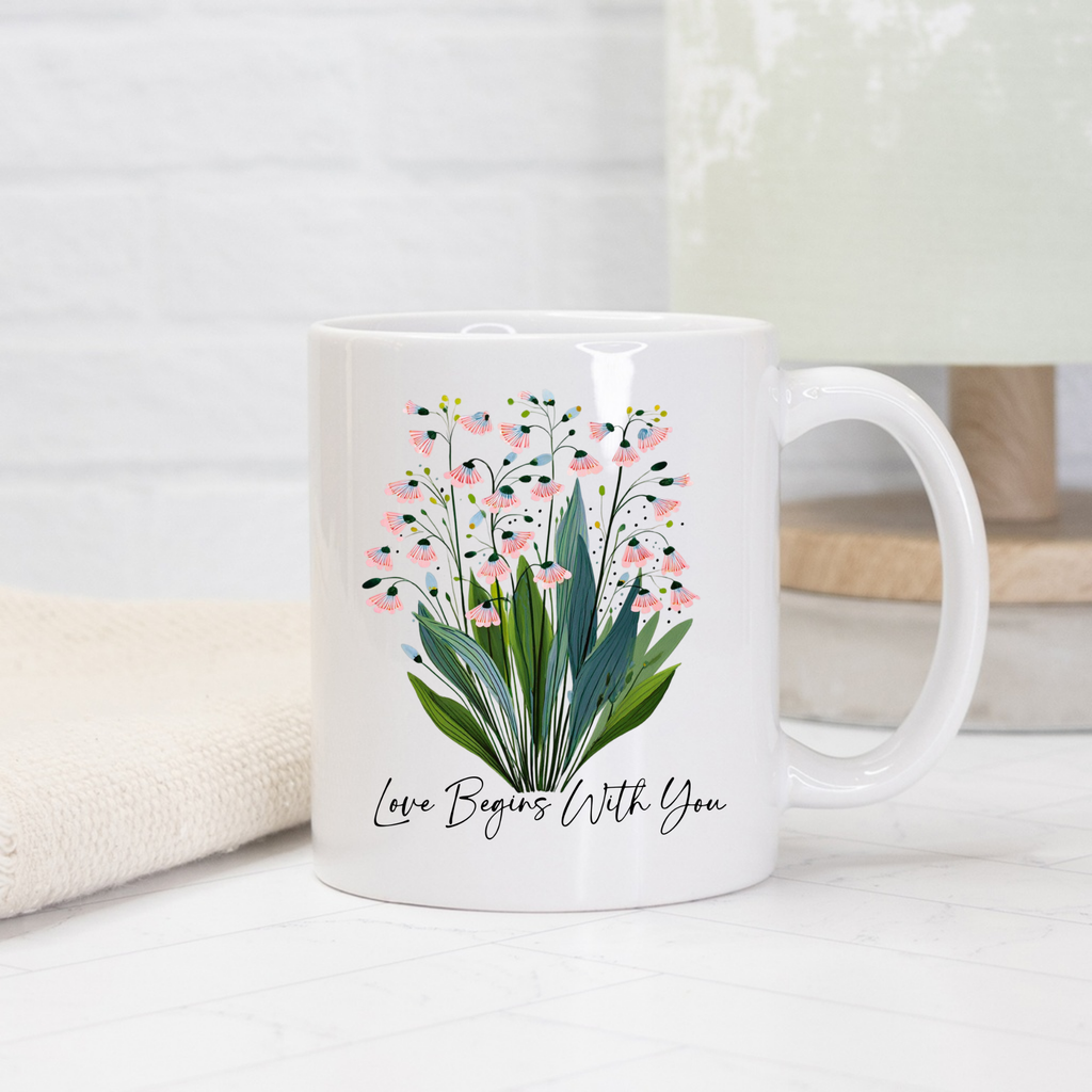 White 11oz. mug with floral design and text 'Love Begins With You' on a light background