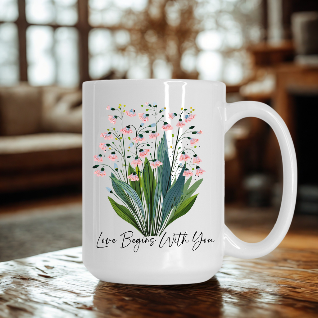 White 15oz. mug with floral design and text 'Love Begins With You' on a wooden surface.