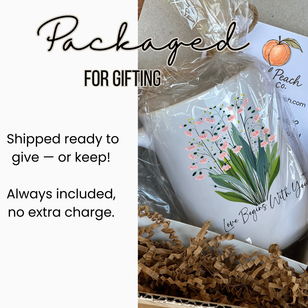 White 15oz. ceramic mug with floral design and text 'Love Begins With You', wrapped in cellophane and in a white gift box with brown paper and tissue.