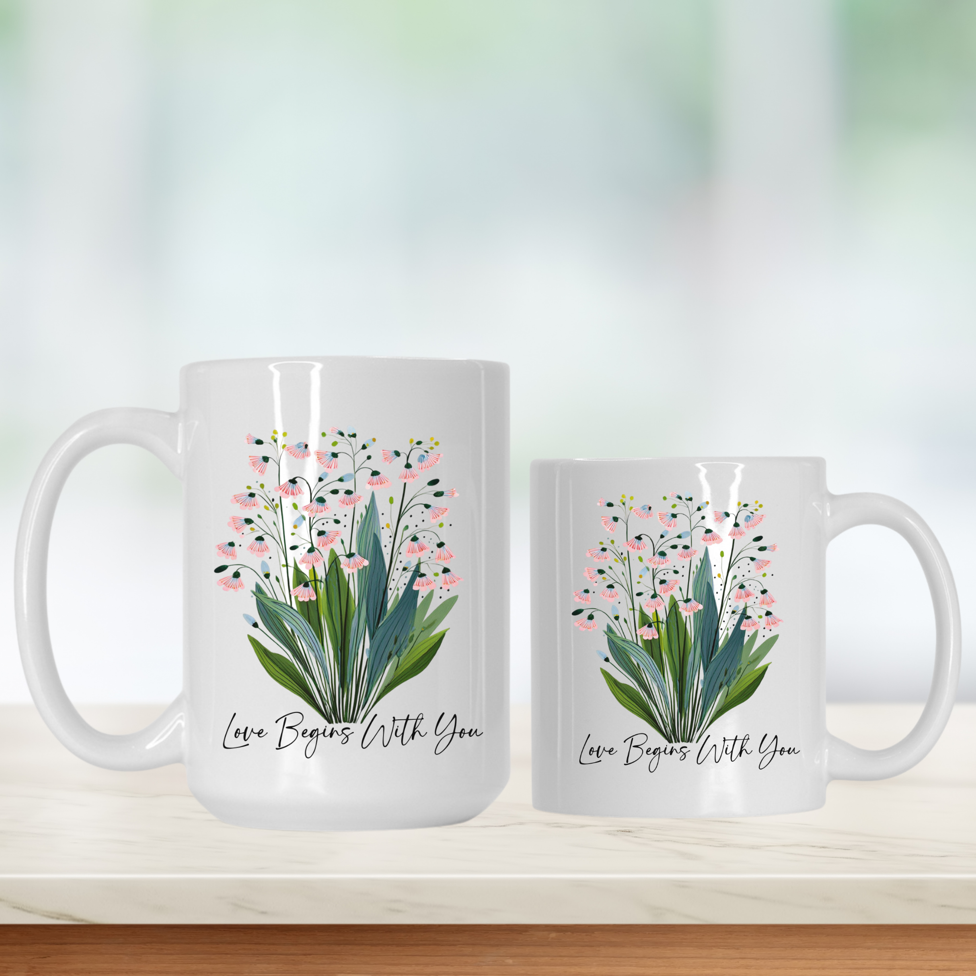 Two white mugs with floral design and 'Love Begins With You' text on a light background