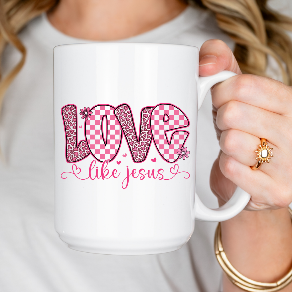 White mug with pink and red text held by a person wearing a gold ring and bracelet.