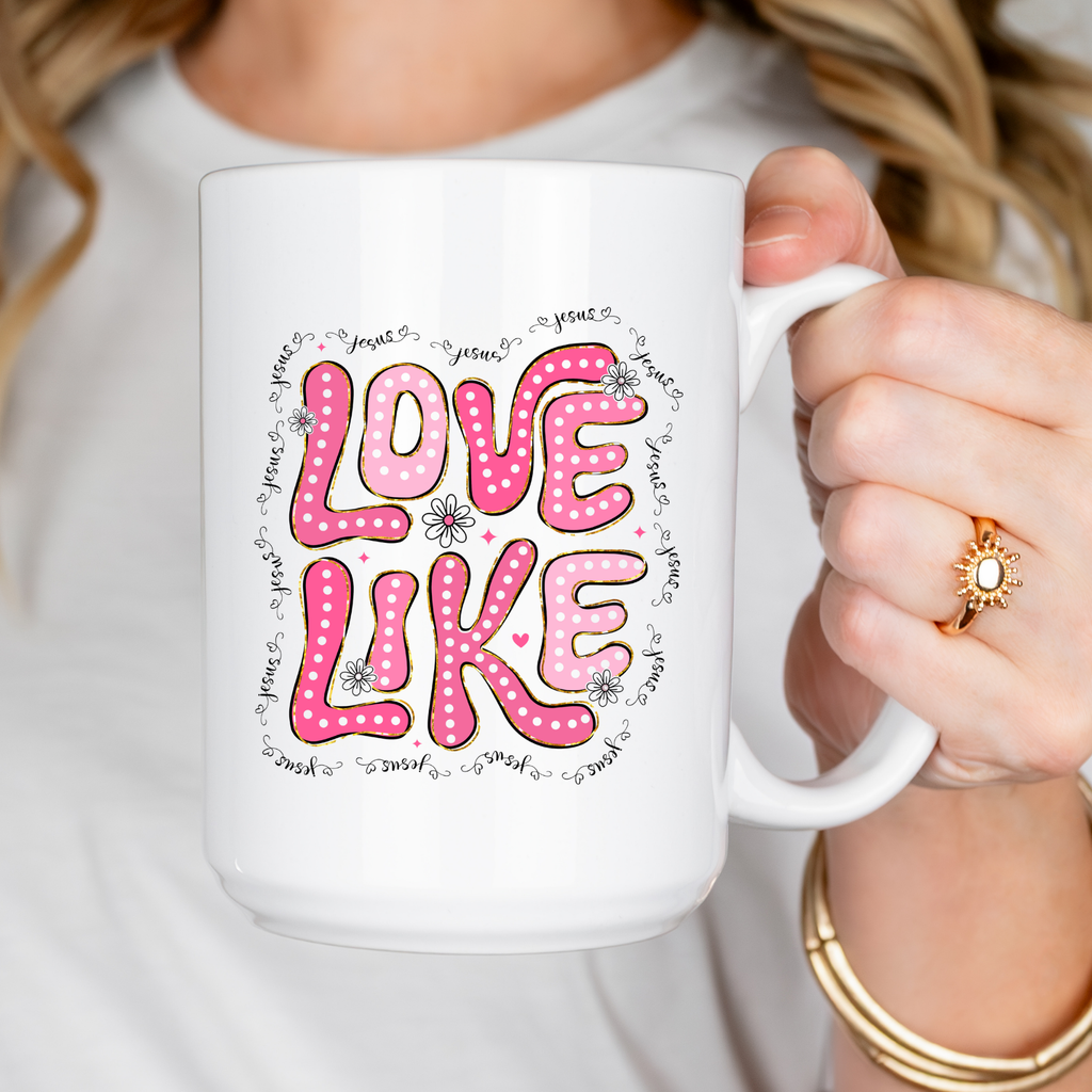 Person holding a white mug with pink 'LOVE LIKE' text design.