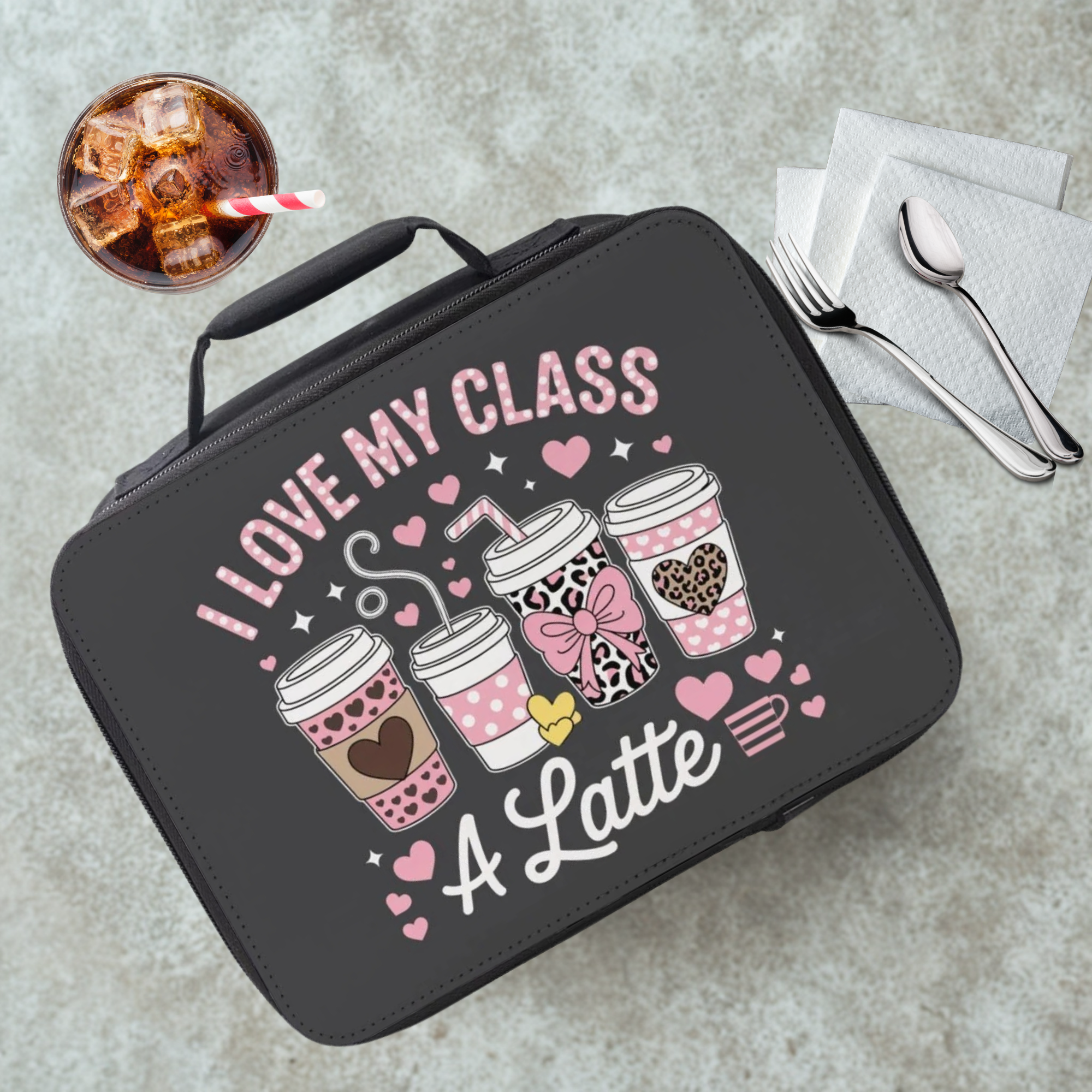 Black lunch bag with 'I love my class a latte' design on a gray table with a drink and utensils.