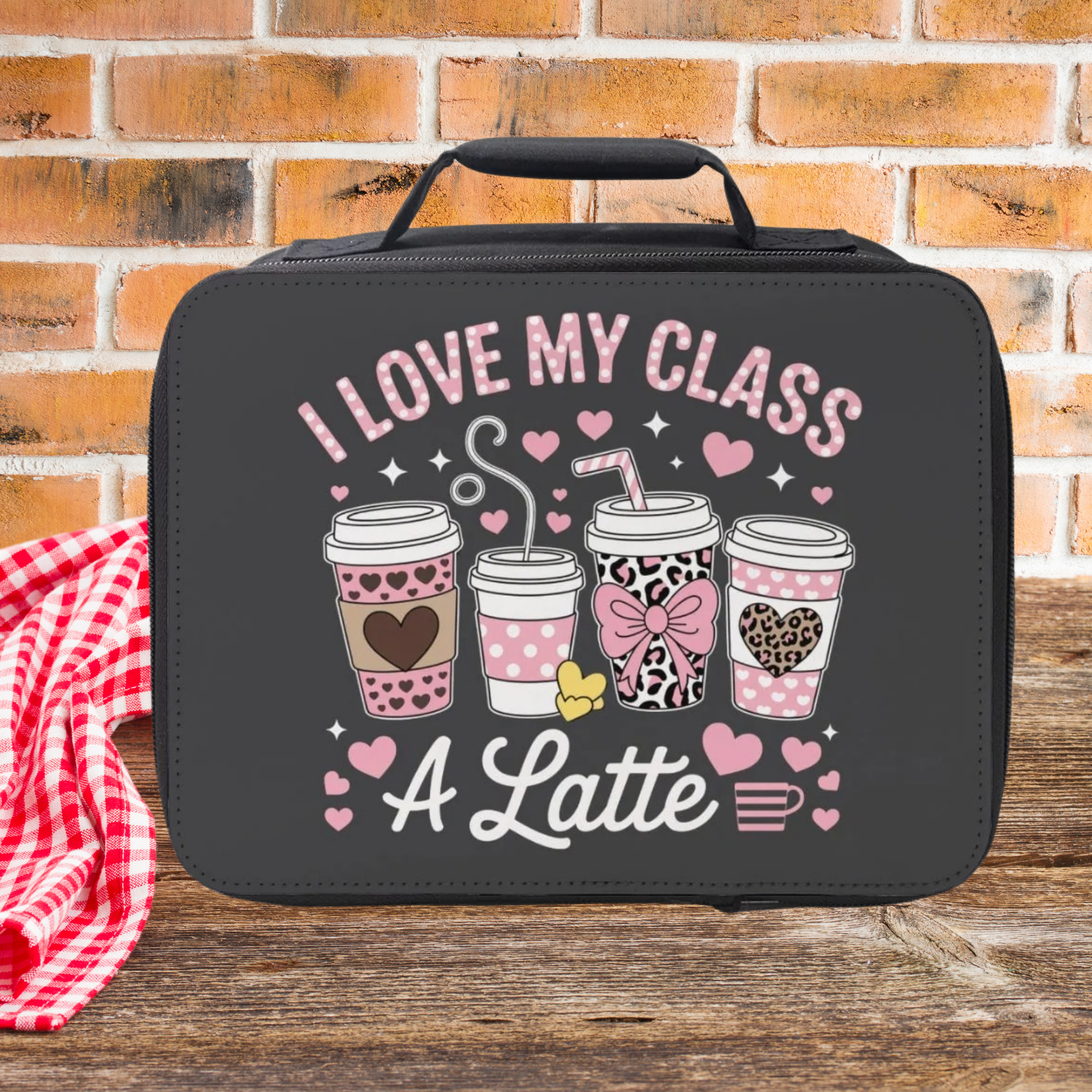 Black lunch bag with 'I love my class a latte' text and coffee cup graphics on a picnic table against a  brick wall background.