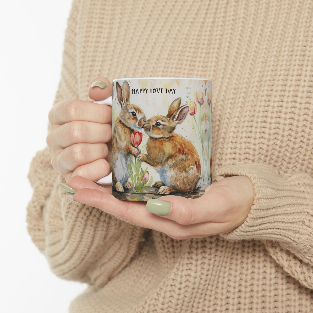 Person holding an 11oz mug with rabbit illustration and 'Happy Love Day' text, wearing a beige sweater.
