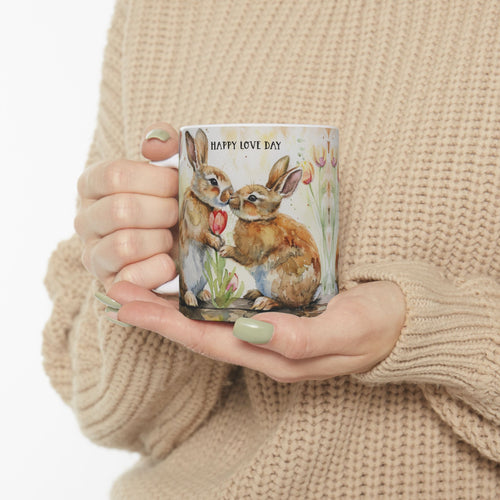 Person holding an 11oz mug with rabbit illustration and 'Happy Love Day' text, wearing a beige sweater.