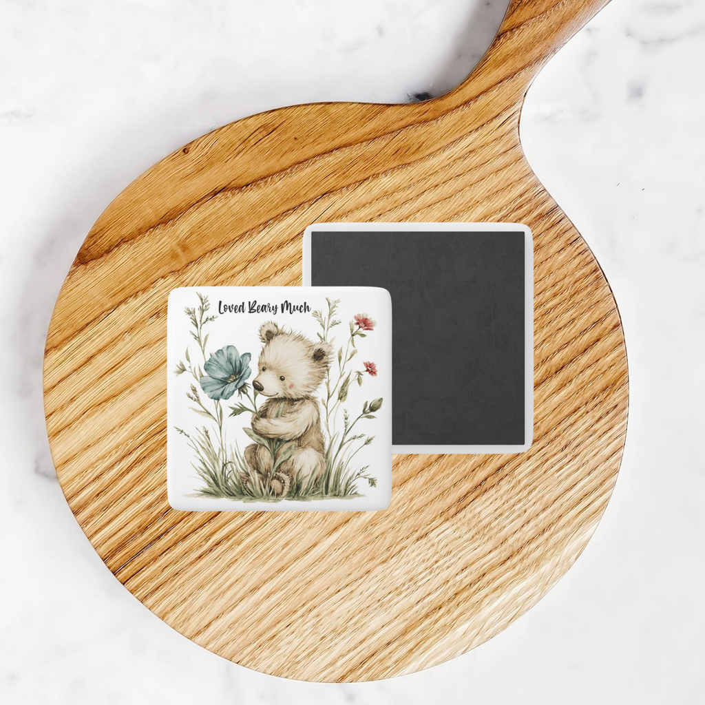 Two square magnets on a wooden board with one featuring a bear and flowers design.