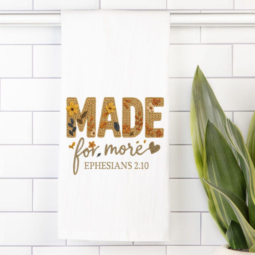 Tea towel with Decorative text 'MADE for more Ephesians 2:10' on a white tiled wall with a plant.