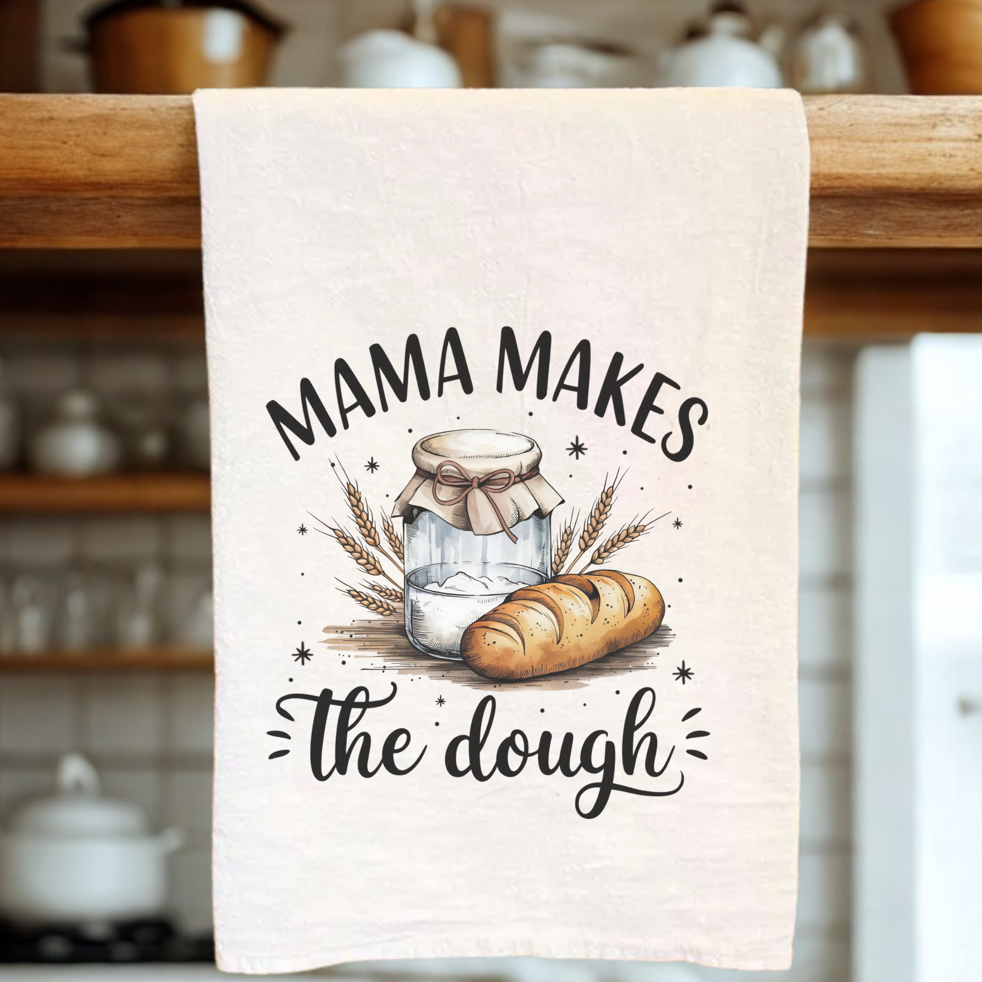 Kitchen towel with bread and jar design and 'Mama Makes the Dough' text on a wooden rack.