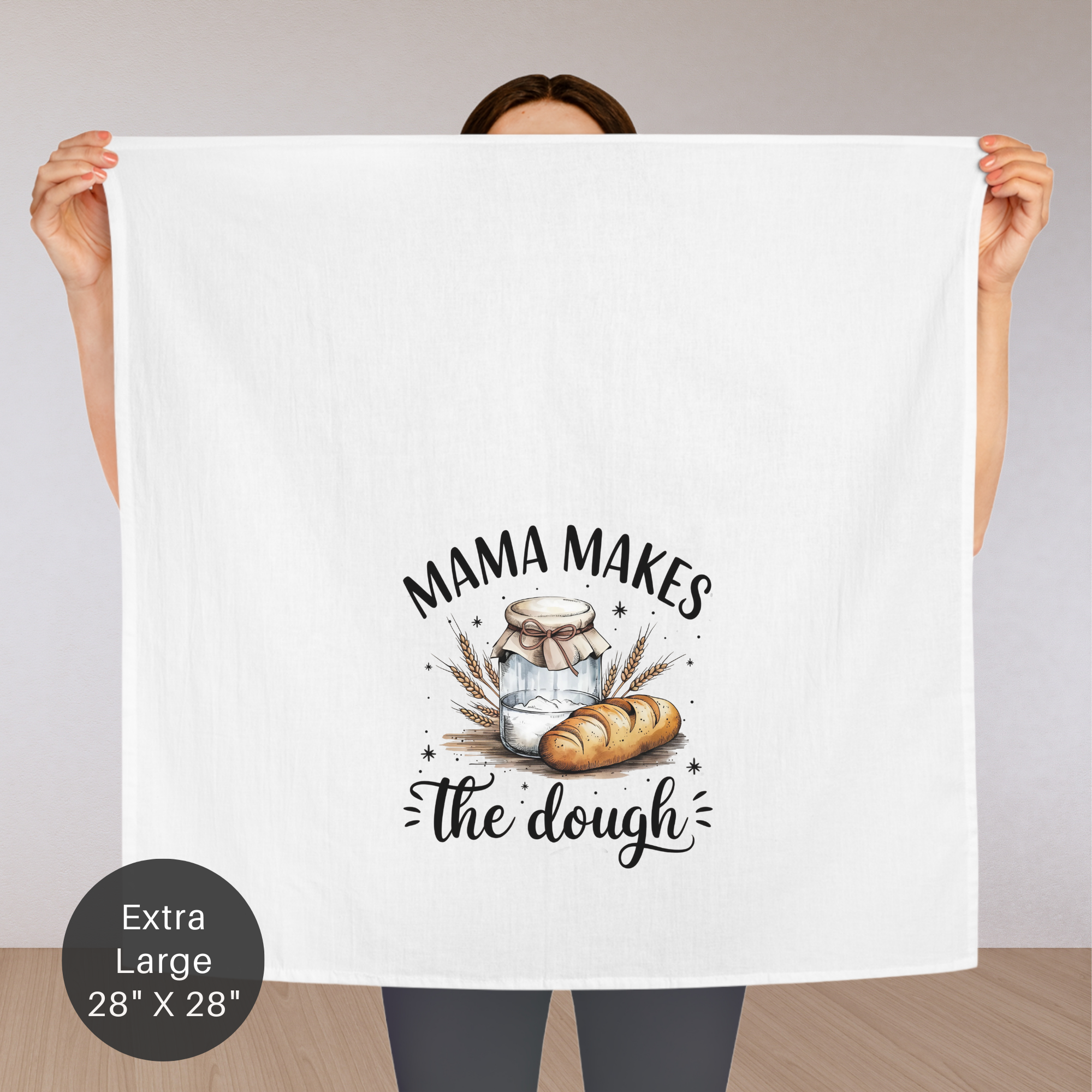 Person holding an extra large white tea towel with 'Mama Makes the Dough' design.