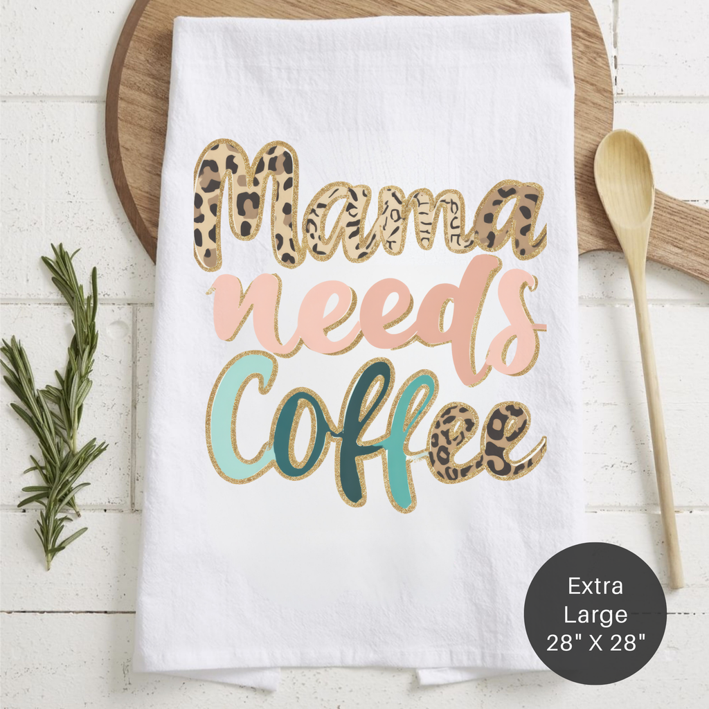 White tea towel with 'Mama needs coffee' text on a wooden surface with a spoon and rosemary.