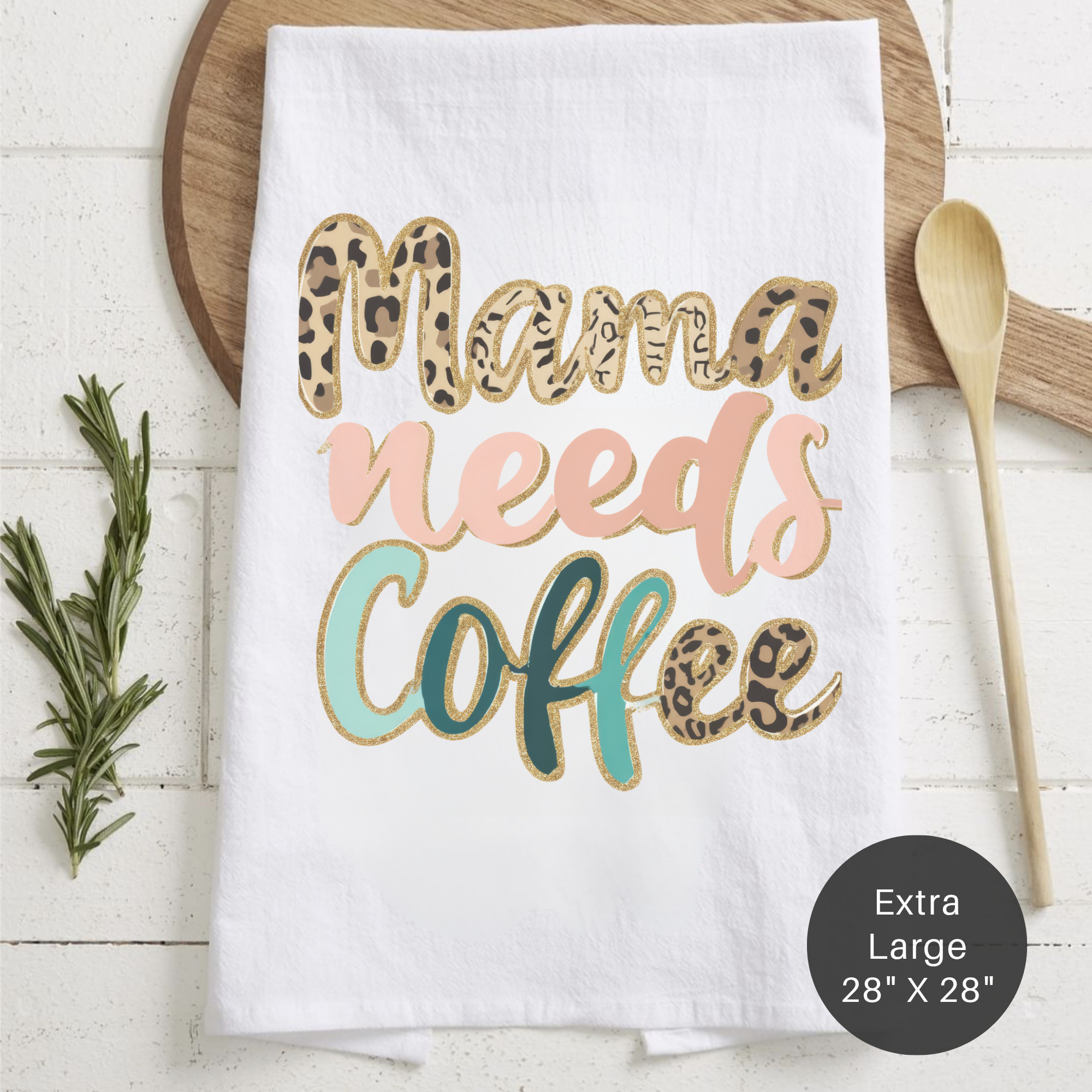 White tea towel with 'Mama needs coffee' text on a wooden surface with a spoon and rosemary.