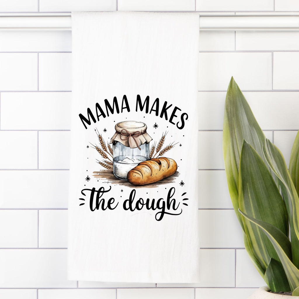 Decorative kitchen towel with bread and jar design and 'Mama Makes the Dough' text on a white tiled wall.