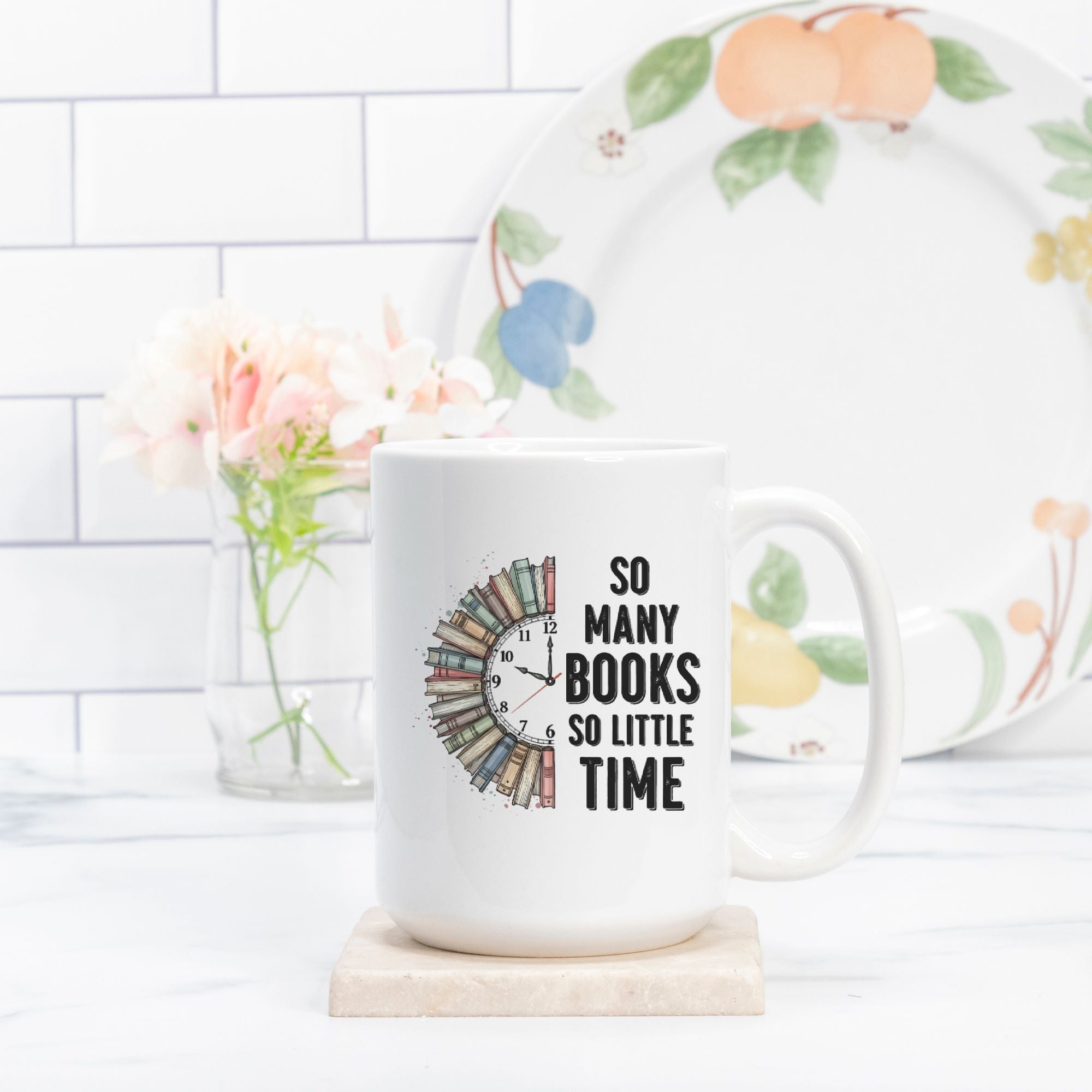 White mug with 'So Many Books So Little Time' text on a white surface with a floral plate in the background.