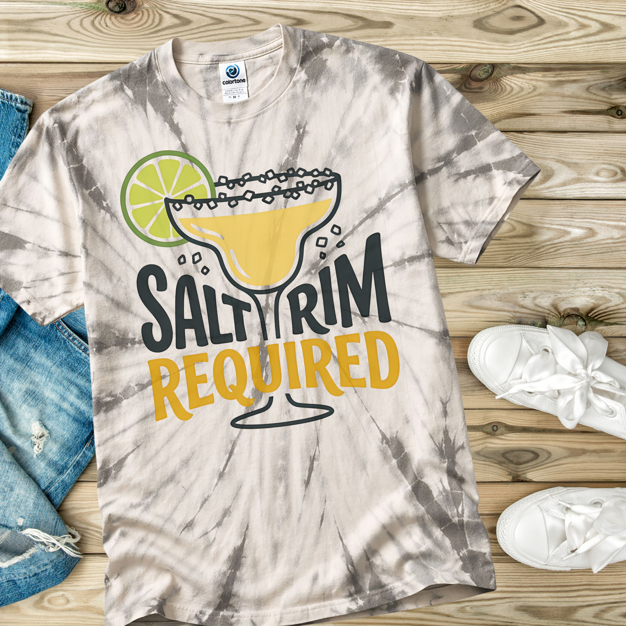 Tie-dye t-shirt in the color Spider Silver with 'Salty Rim Required' graphic on a wooden surface with jeans and sneakers.