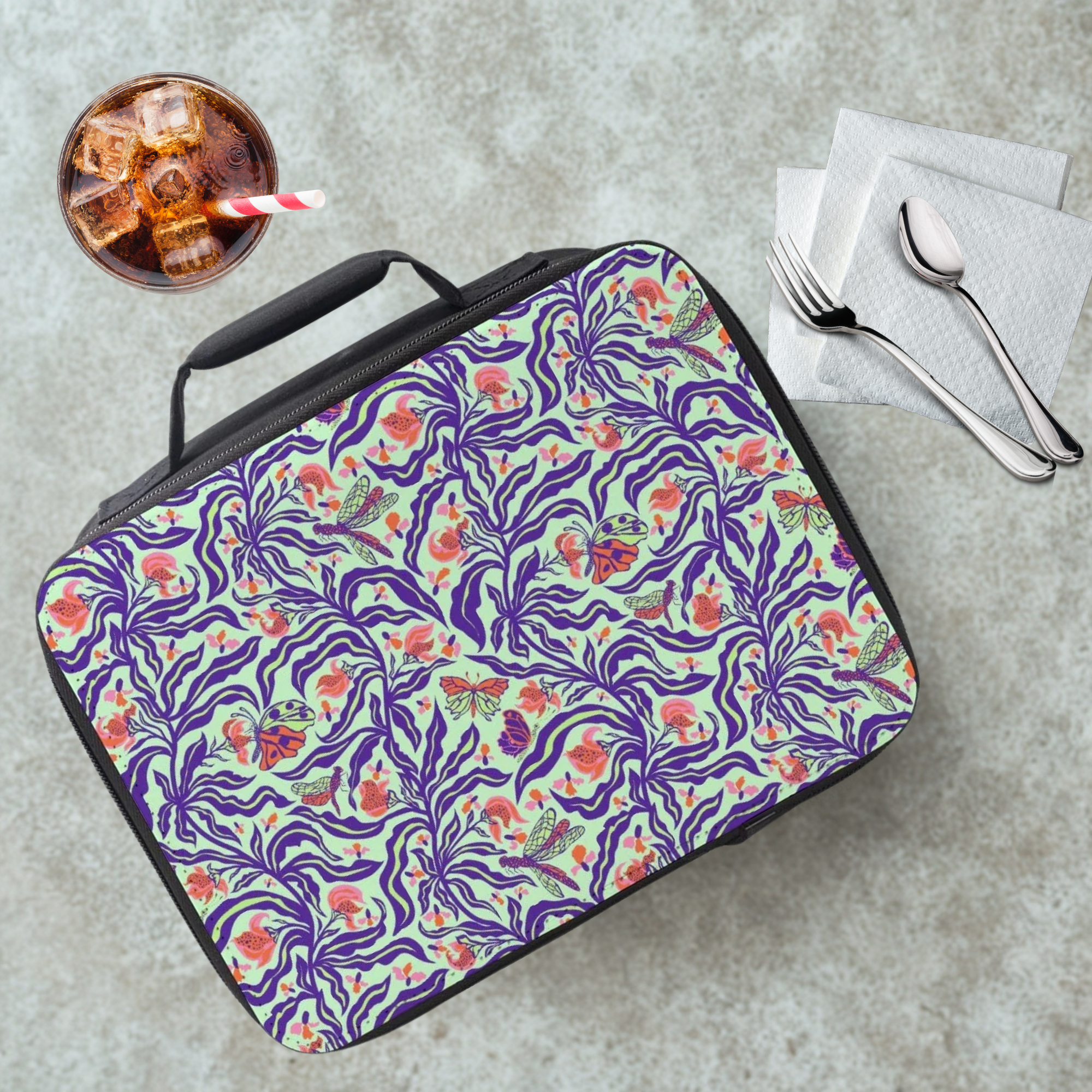 Floral patterned lunch bag on a cafeteria table with a drink and utensils.