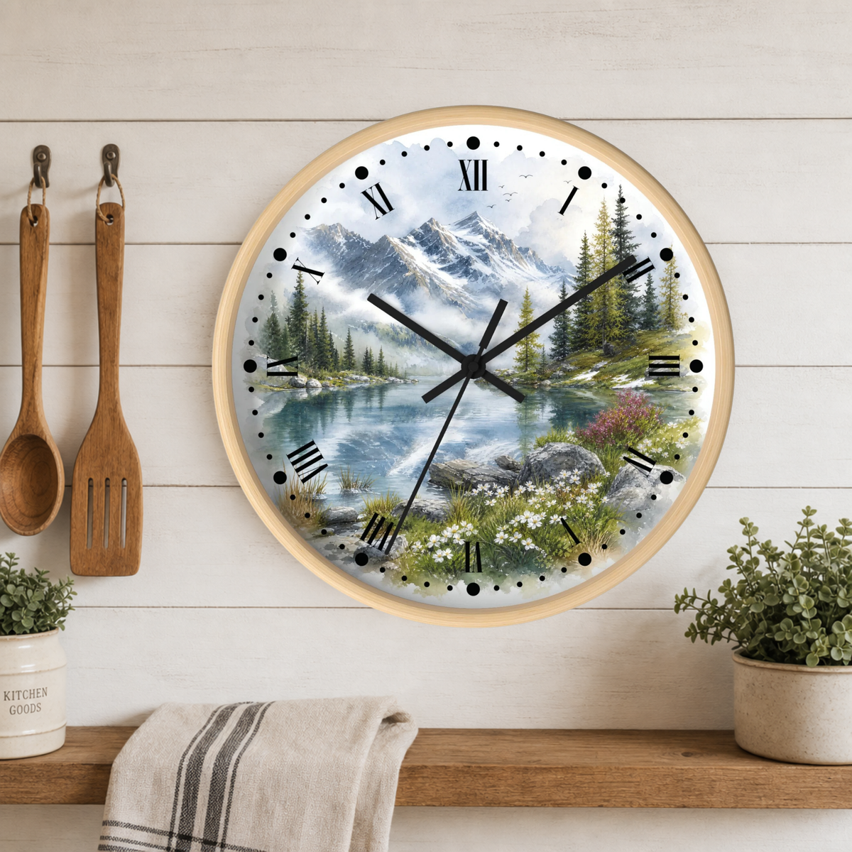Round wall clock with a scenic mountain lake print, mounted on a white wood plank kitchen wall above a shelf with plants and utensils.