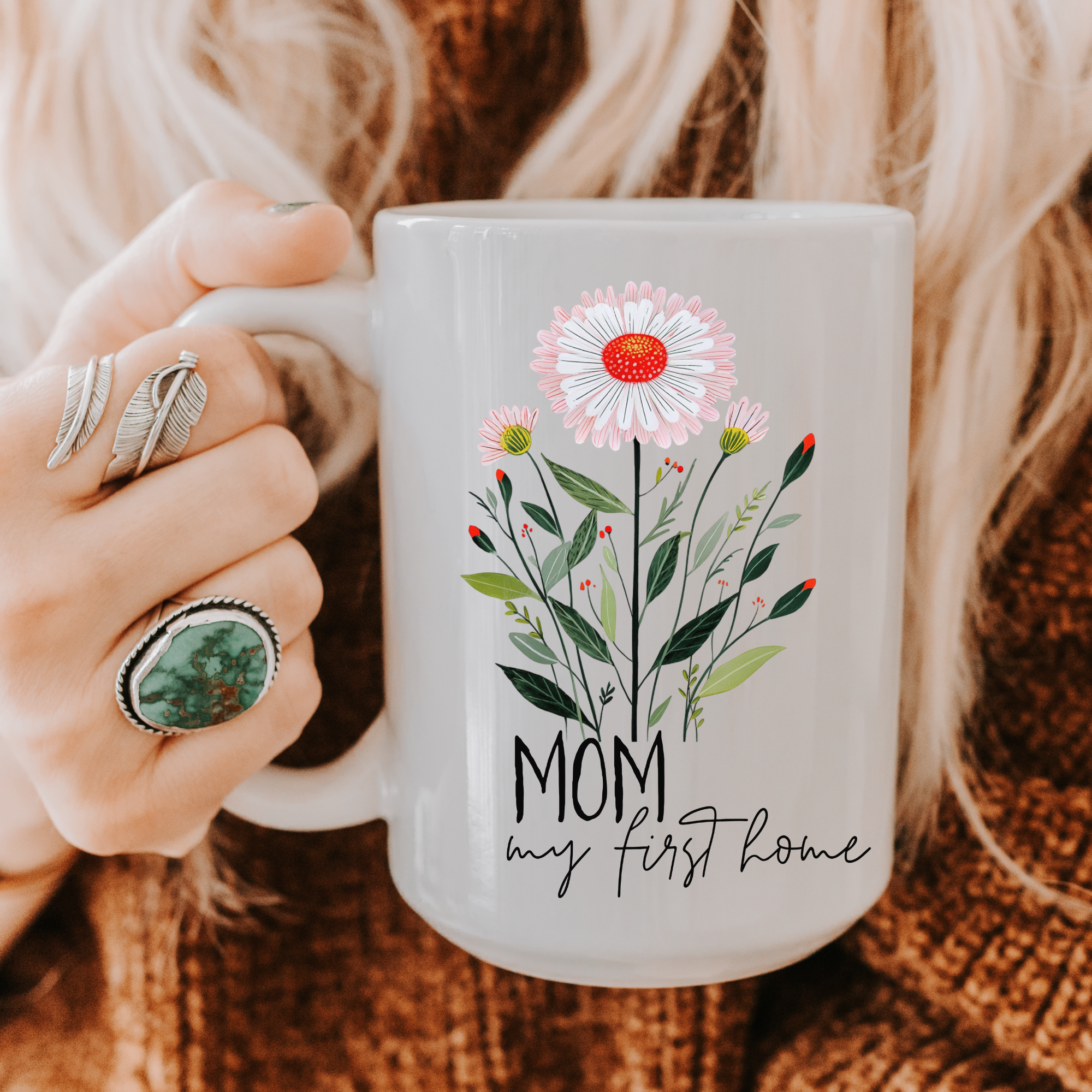 Person holding an 11oz mug with floral design and text, wearing rings.
