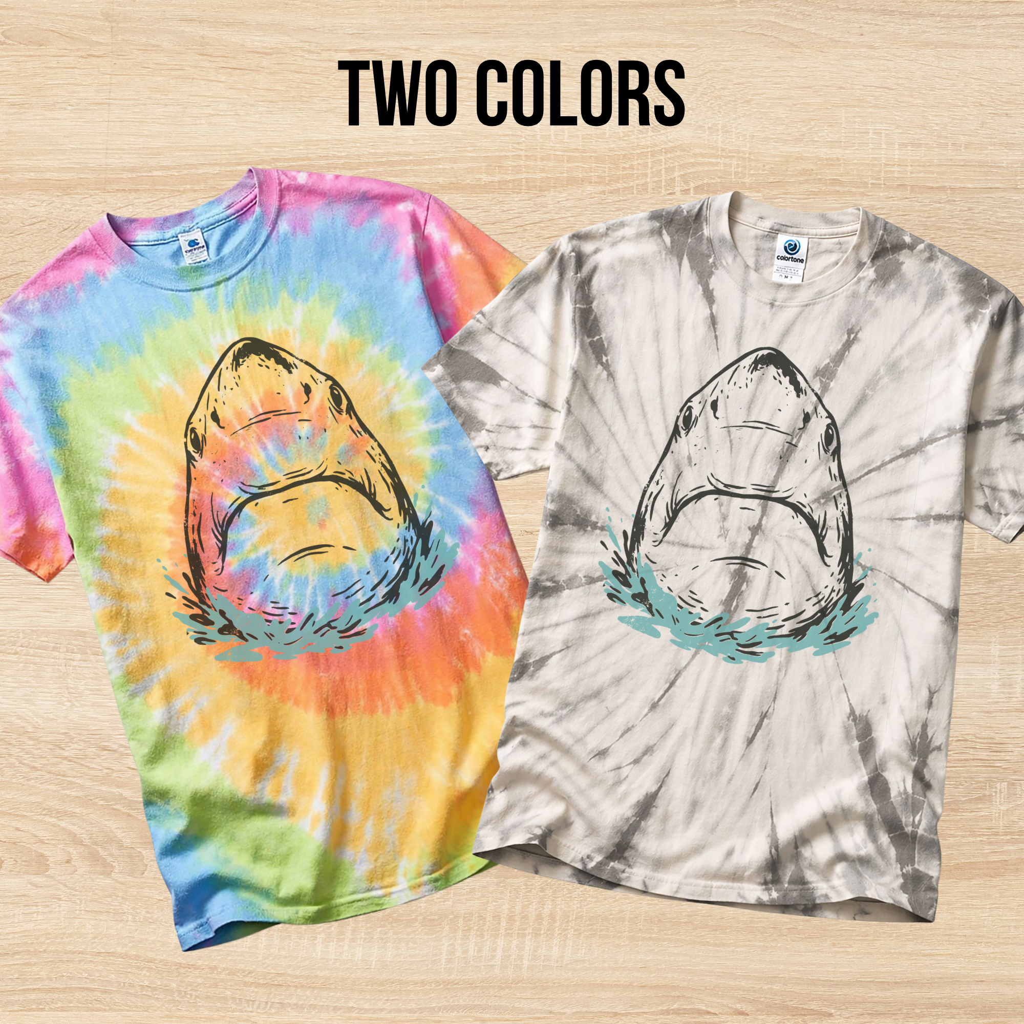 Two tie-dye t-shirts in the colors Eternity and Spider Silver with hand drawn shark designs on a wooden surface.