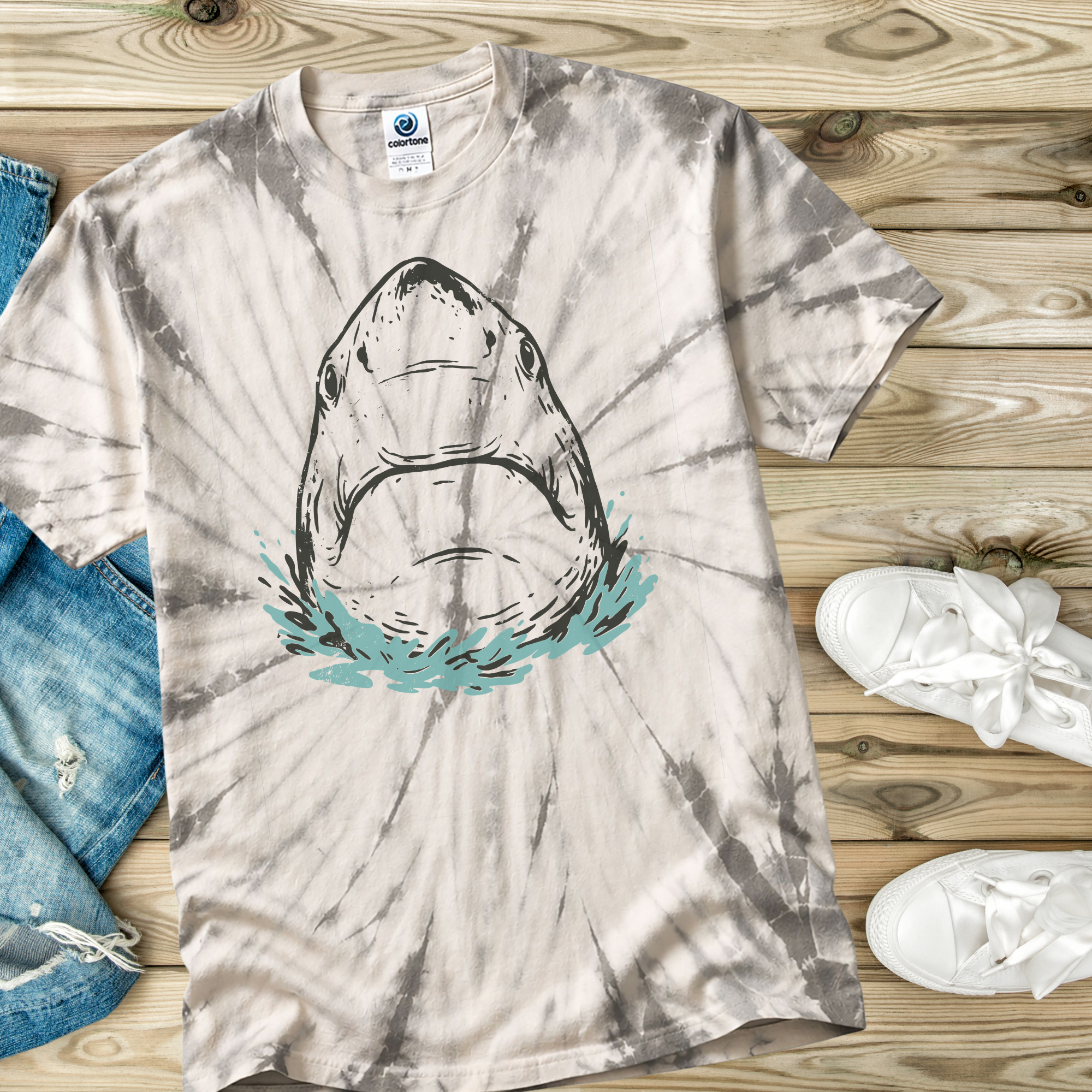 Tie-dye t-shirt in the color Spider Silver with a hand drawn shark design on a wooden surface with jeans and sneakers.