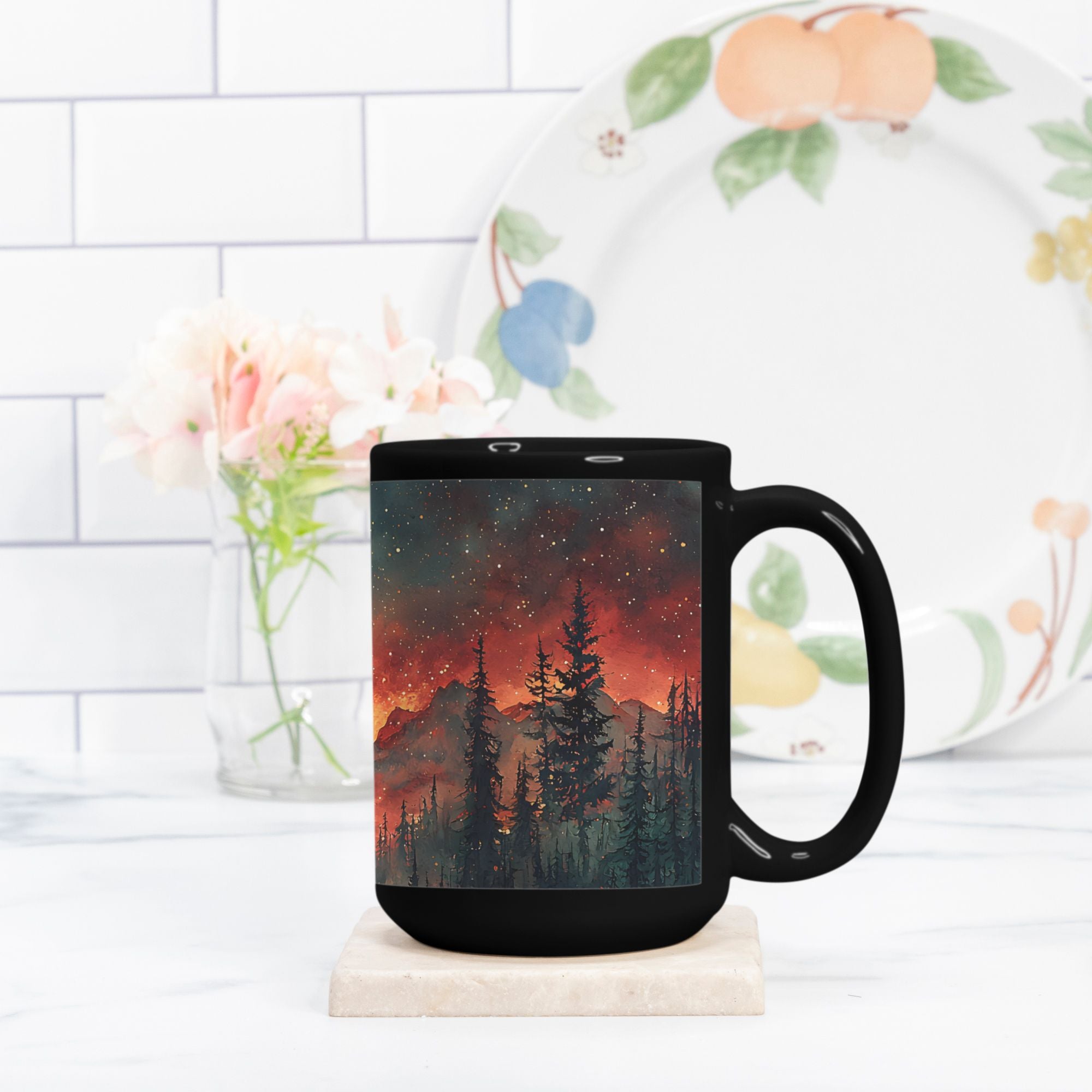 Black mug with a scenic design of trees and mountains on a white surface.