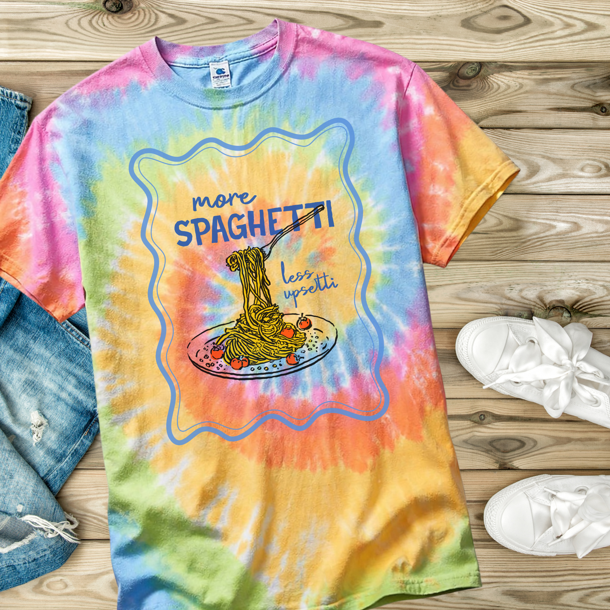 Colorful tie-dye t-shirt with a graphic of spaghetti and text on a wooden surface.