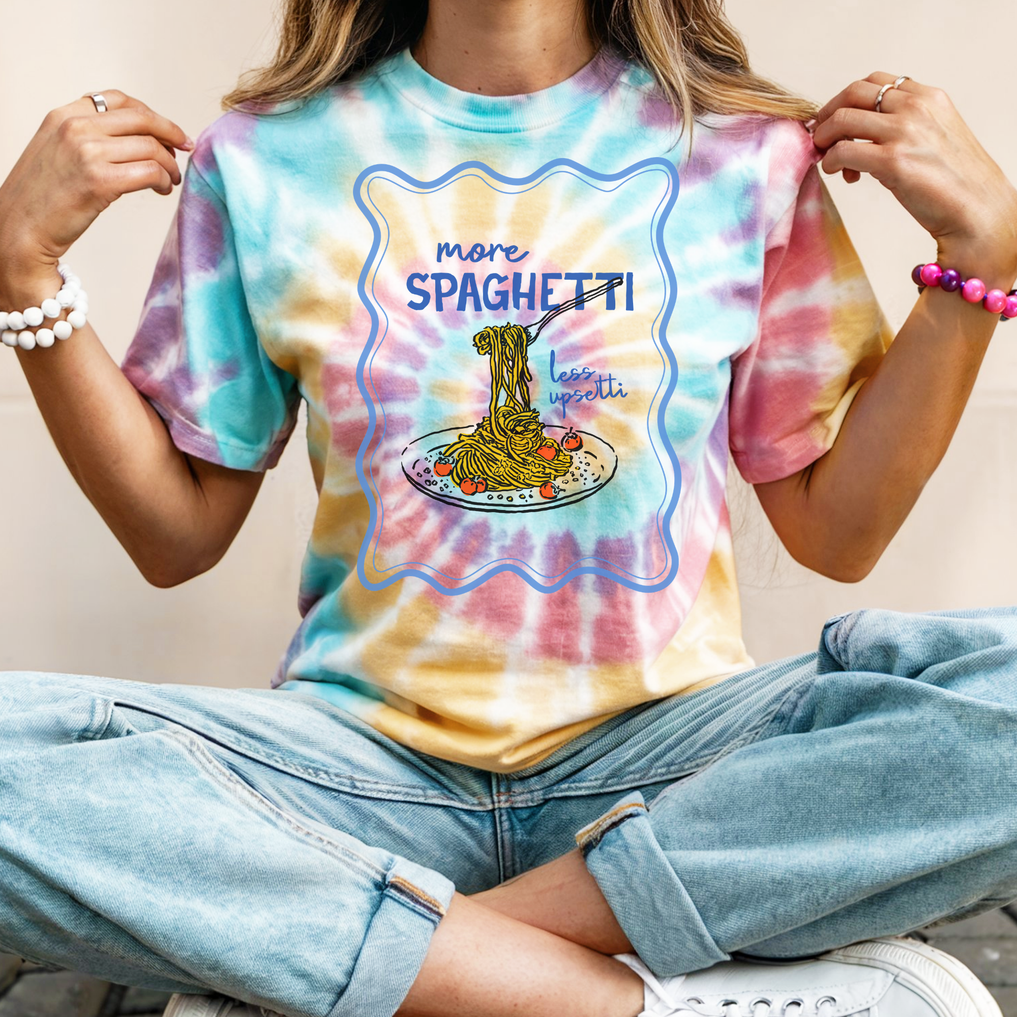 Person wearing a tie-dye t-shirt with a graphic design of spaghetti and text.