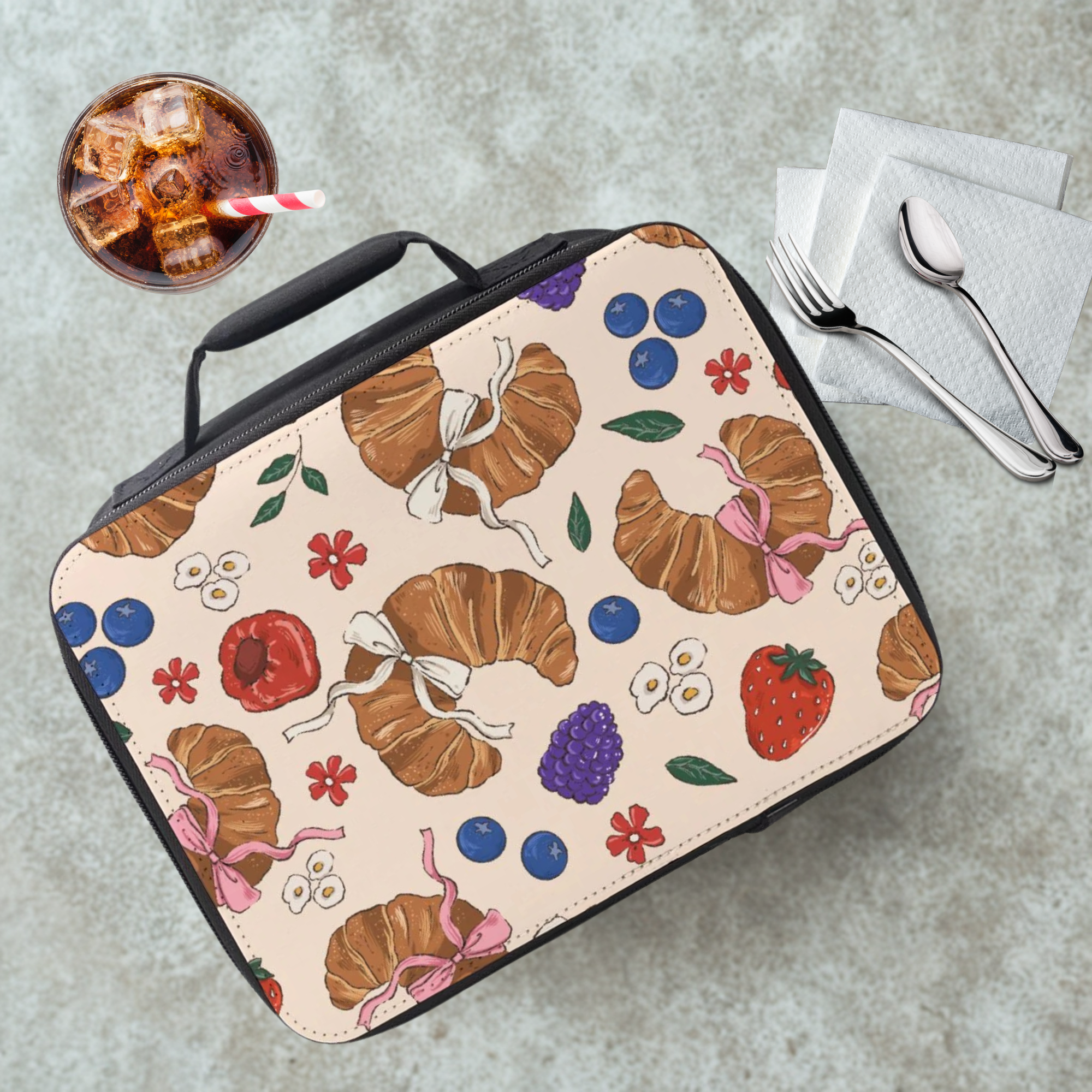 Lunch bag with pastry and fruit pattern on a cafeteria table with a drink and utensils.