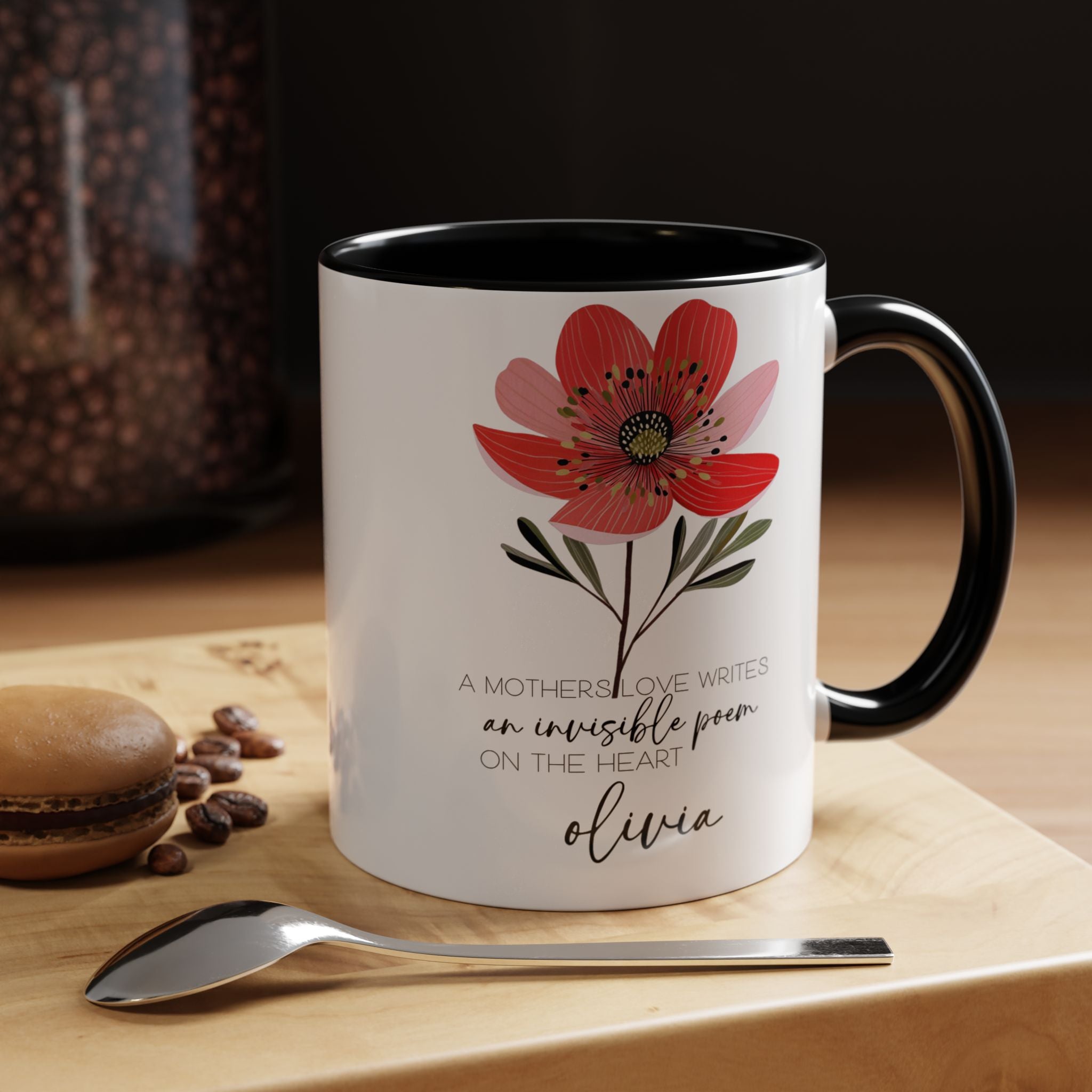 Black accent mug with floral design and text on a wooden surface with coffee beans and a spoon.