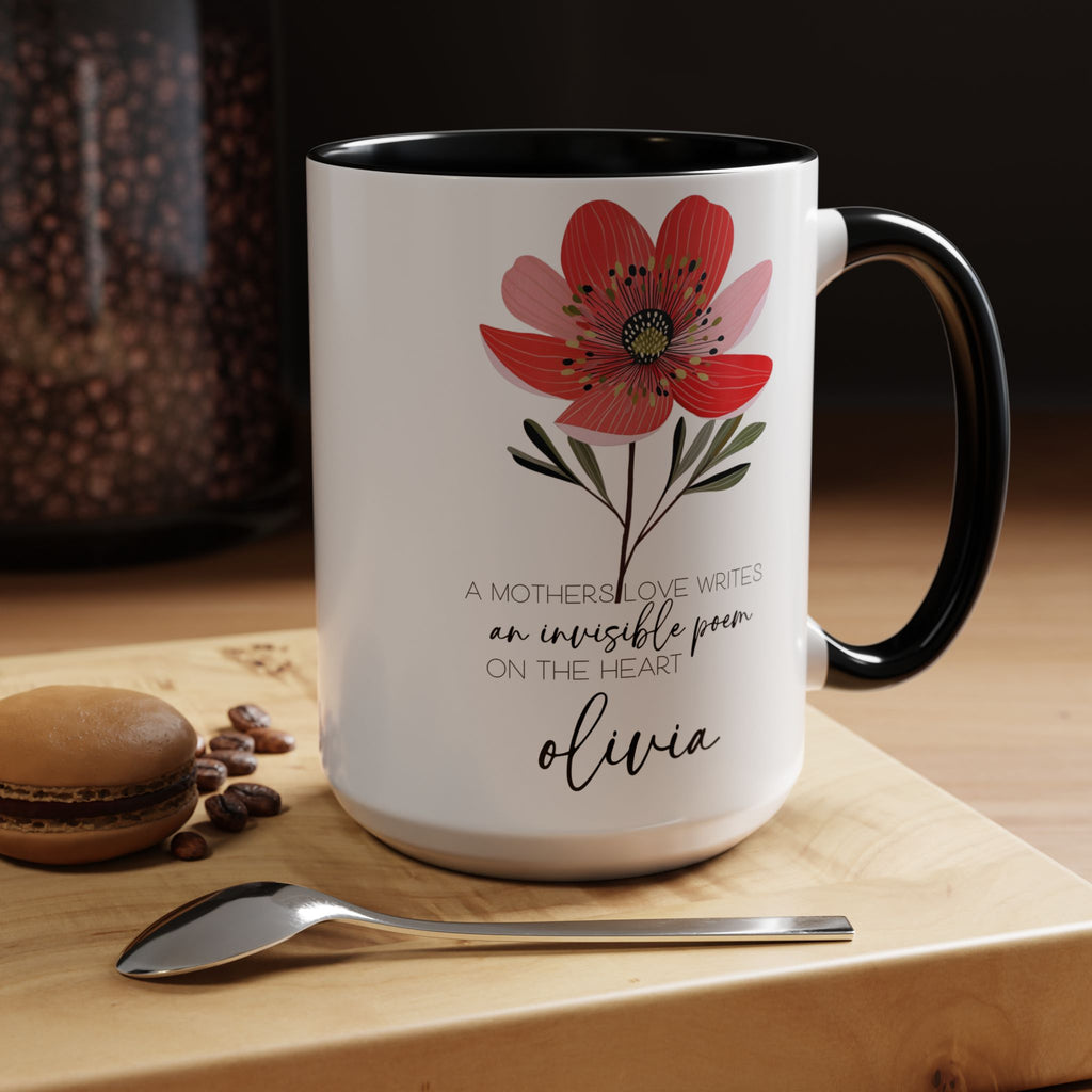 White mug with red floral design and text on a wooden surface with coffee beans and a macaron.
