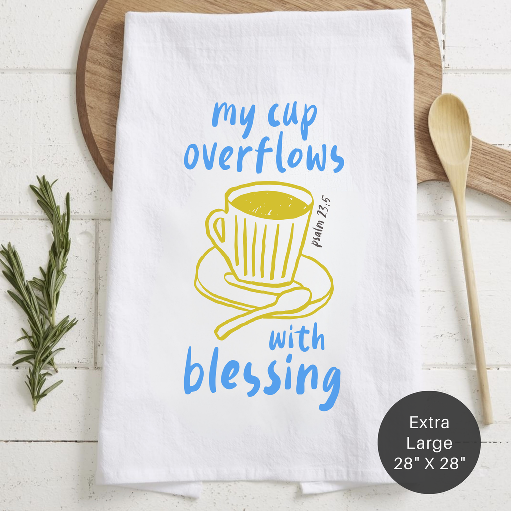 White towel with yellow and blue design featuring a cup and text, placed on a wooden surface.