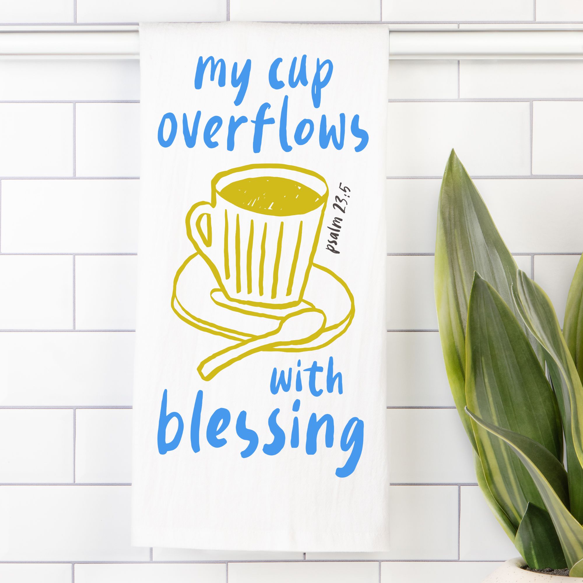 Decorative tea towel with a cup and saucer illustration and text on a white tiled wall.